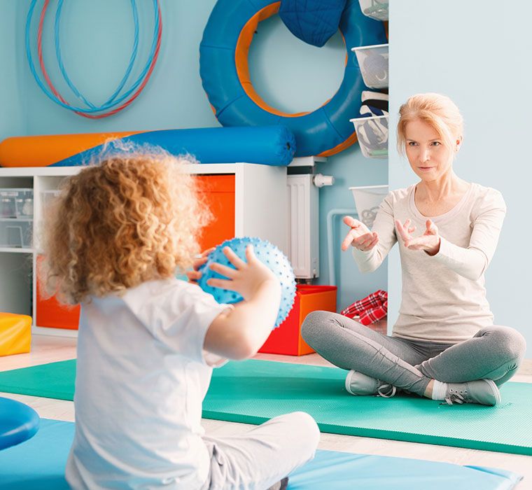 Ein Kind wirft einen Ball zur Physiotherapeutin - Behandlung nach Bobath